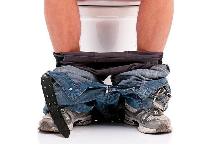 Heruntergelassene Hose von Mann auf Toilette.