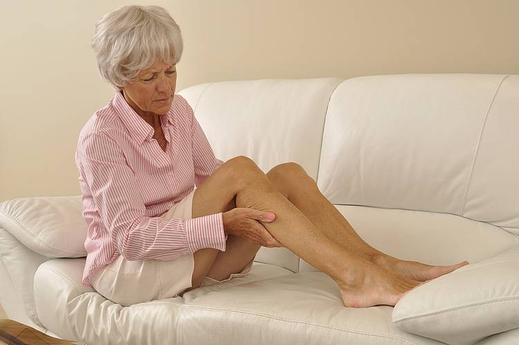 Seniorin auf Sofa massiert Bein mit Wadenkrämpfen