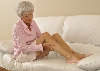 Seniorin auf Sofa massiert Bein mit Wadenkrämpfen