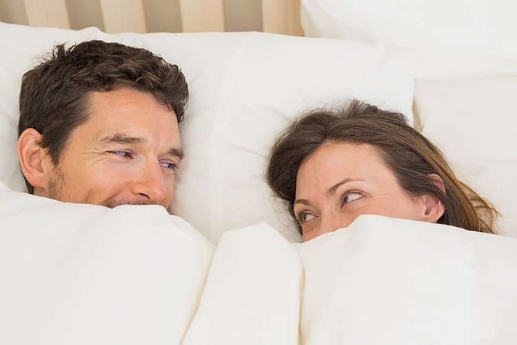 Mann und Frau ziehen sich die Bettdecke bis zur Nase hoch