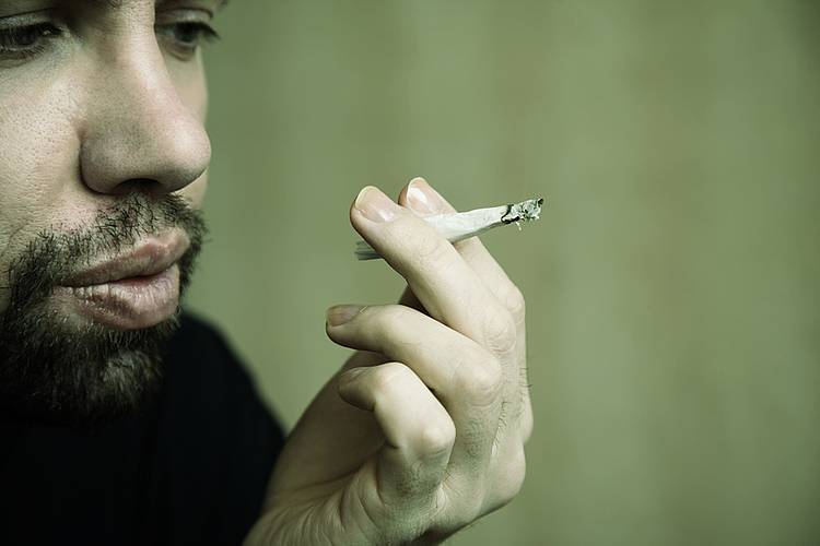 Junger Mann mit Bart raucht einen Joint.