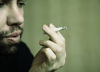 Junger Mann mit Bart raucht einen Joint.