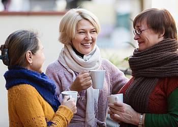 Frauen mit Schal und Jacke trinken Tee auf Terrasse