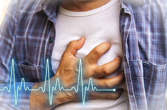 Junger Mann fasst sich an den Brustkorb, weil er zum Beispiel einen Herzinfarkt erleidet.