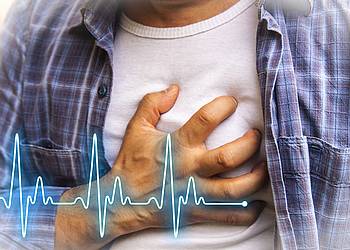 Junger Mann fasst sich an den Brustkorb, weil er zum Beispiel einen Herzinfarkt erleidet.