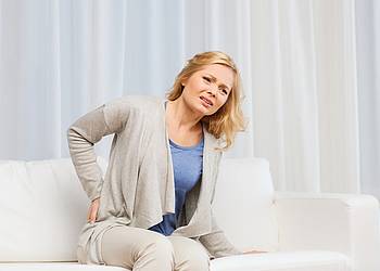 Blonde Frau auf Sofa hält sich die schmerzenden Nieren