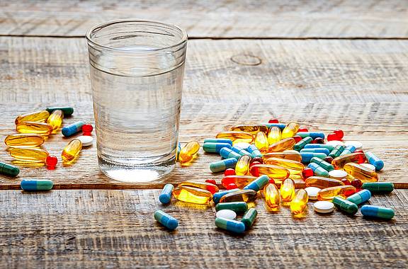 Wasserglas umgeben von verschiedenen Antibiotika-Tabletten