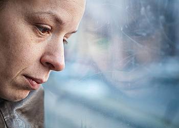 Frau lehnt erschöpft Kopf an Fensterscheibe