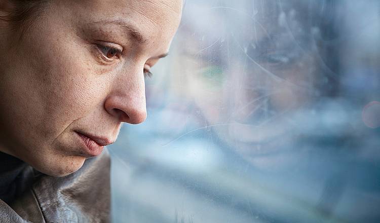 Frau lehnt erschöpft Kopf an Fensterscheibe