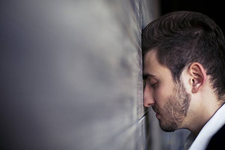 Mann lehnt erschöpft seinen Kopf gegen eine Wand