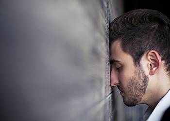 Mann lehnt erschöpft seinen Kopf gegen eine Wand