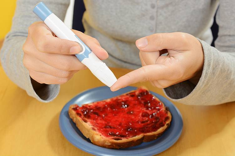 Person misst eigenen Blutzuckerspiegel mit Blutzuckermessgerät am Finger