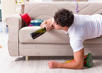 Junger Mann liegt nach Kanrevalsparty betrunken auf dem Sofa