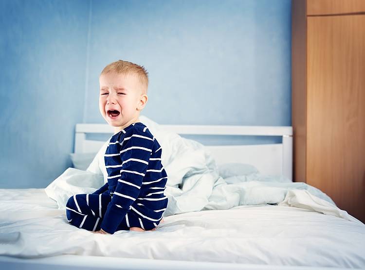 Kleiner Junge mit Bauchweh sitzt auf Bett