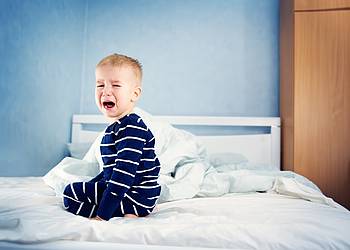 Kleiner Junge mit Bauchweh sitzt auf Bett