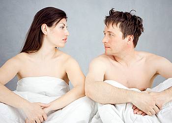 Junges Paar im Bett diskutiert über Vorsorge für sexuelle Gesundheit