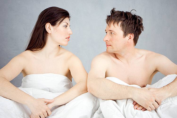 Junges Paar im Bett diskutiert über Vorsorge für sexuelle Gesundheit