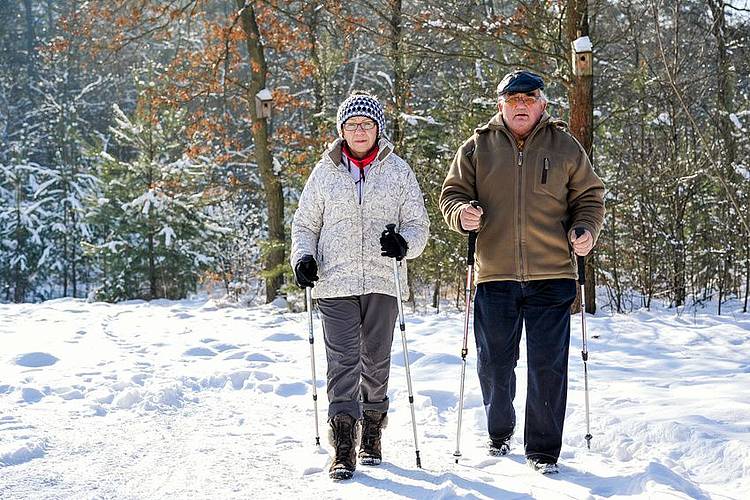 Ein Rentnerpaar macht eine Schneewanderung mit Gehstöcken.