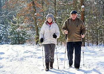 Ein Rentnerpaar macht eine Schneewanderung mit Gehstöcken.