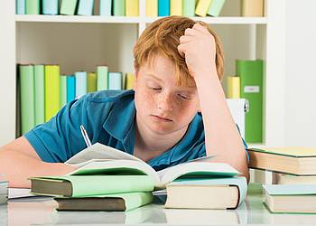 Junge sitzt überfordert über Schulbüchern, weil er sich wegen Bluthochdruck schlecht konzentrieren kann. 