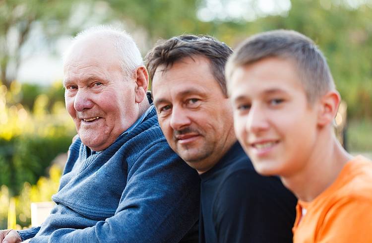 Vater, Sohn und Enkel sitzen nebeneinander in einem Garten.
