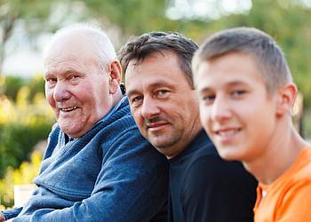 Vater, Sohn und Enkel sitzen nebeneinander in einem Garten.