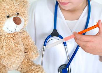 Eine Ärztin gibt einem Teddybär eine Imfung. 