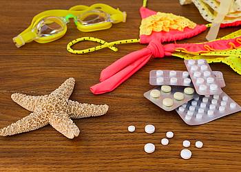 Tablettenblister liegen neben Seestern, Bikini und Schwimmbrille