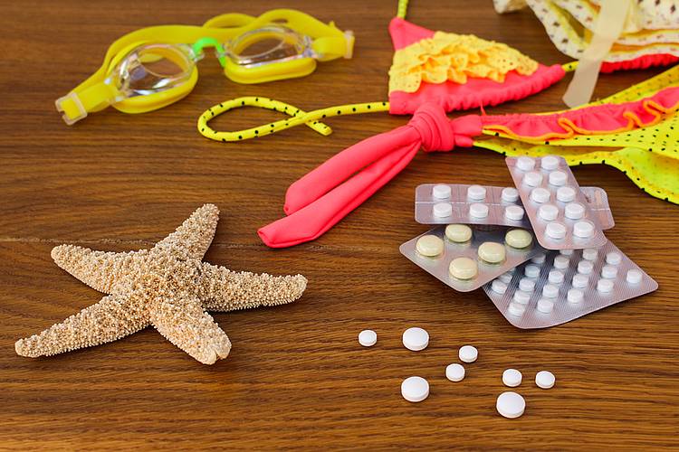 Tablettenblister liegen neben Seestern, Bikini und Schwimmbrille