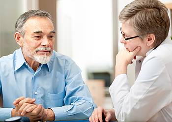 Älterer Mann lässt sich von Ärztin zu Behandlung bei Prostatakrebs beraten.