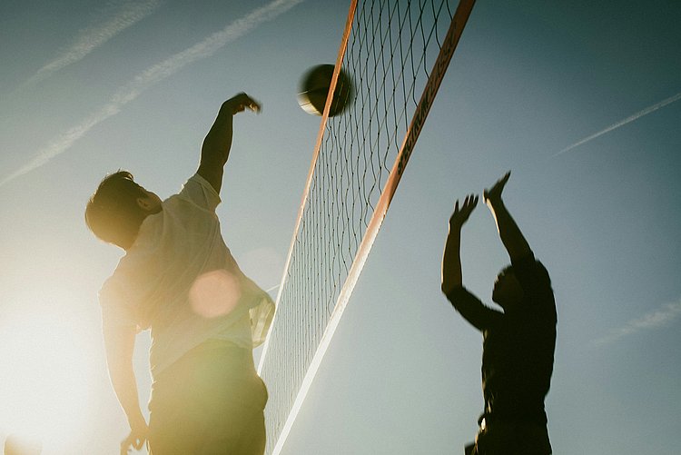 Das Foto zeigt zwei junge Männer beim Beachvolleyball im Gegenlicht.