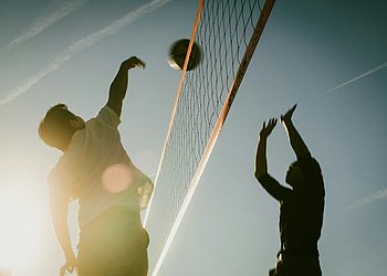 Das Foto zeigt zwei junge Männer beim Beachvolleyball im Gegenlicht. 
