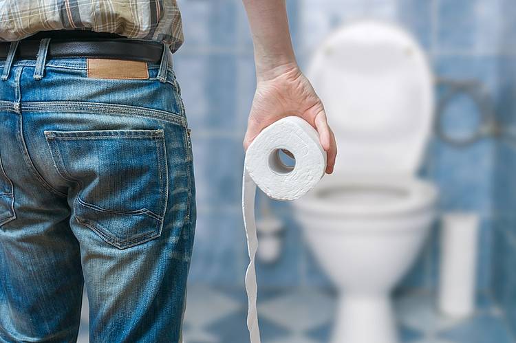 Mann mit Klopapierrolle im Badezimmer vor der Toilette