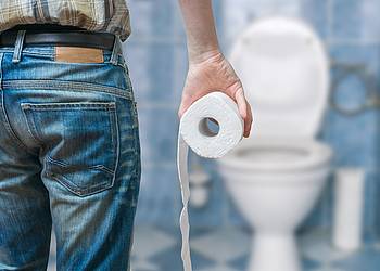 Mann mit Klopapierrolle im Badezimmer vor der Toilette