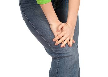 Teilansicht einer Frau mit Rheuma-Schmerzen im Kniegelenk.