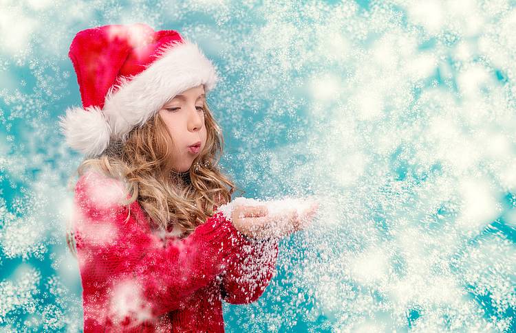 Mädchen in Weihnachtsmannkostüm pustet Schneeflocken