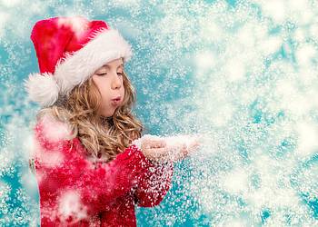 Mädchen in Weihnachtsmannkostüm pustet Schneeflocken