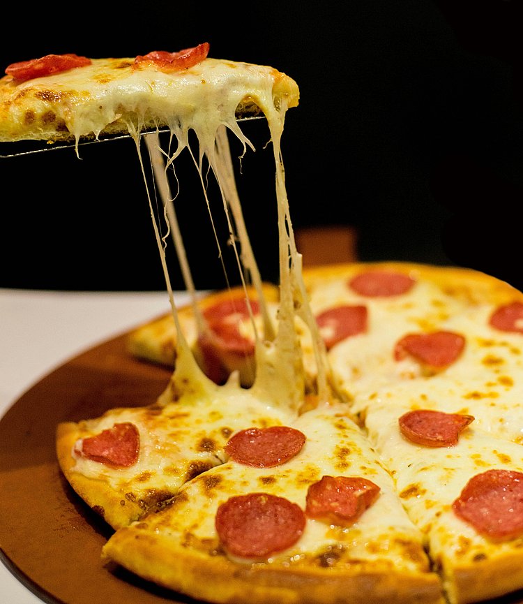 Das Foto zeigt eine Pizza mit Salami und fettigem Käse vor einem schwarzen Hintergrund. 