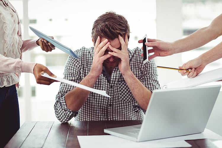 Überforderter Mann am Tisch vor dem Laptop