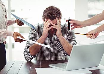 Überforderter Mann am Tisch vor dem Laptop