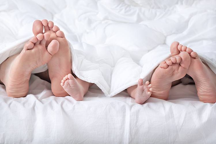 Nackte Füße von Mann, Frau und Baby schauen unter einer Decke hervor. 