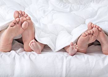 Nackte Füße von Mann, Frau und Baby schauen unter einer Decke hervor. 