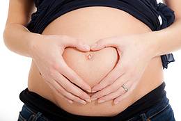 Schwangere Frau hält Hände in Herzform auf den Bauch. 
