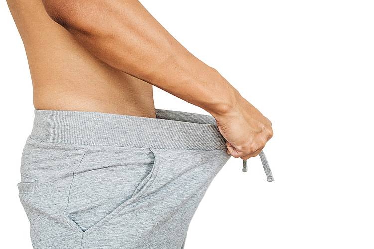 Junger Mann hält sich Jogginghose vom Unterleib weg.