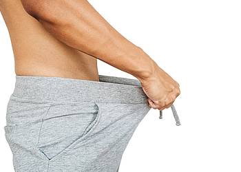 Junger Mann hält sich Jogginghose vom Unterleib weg.