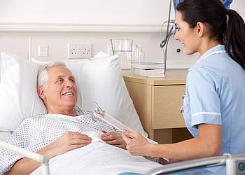 Patient im Krankenhausbett bespricht Blutwerte mit Ärztin.