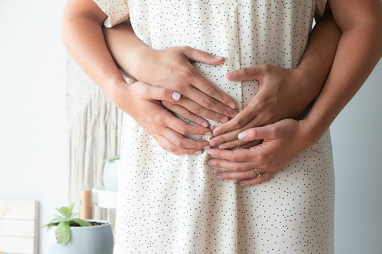 Das Foto zeigt im Bildausschnitt den Bauch einer schwangeren Frau. Vater und Mutter haben schützen die Hände über den Bauch gelegt.