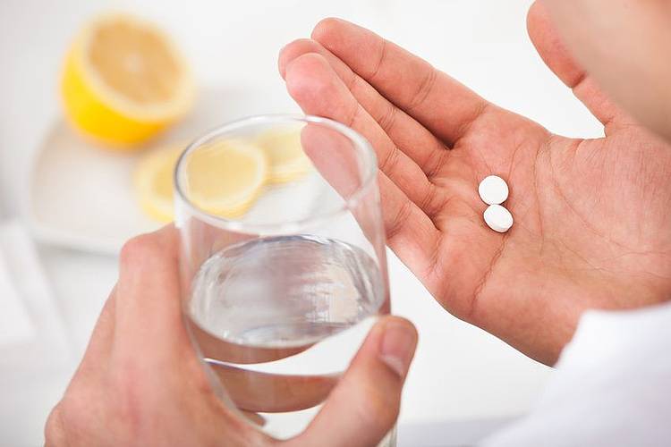 Frauenhände halten Antibiotika-Tabletten und ein Glas Wasser.