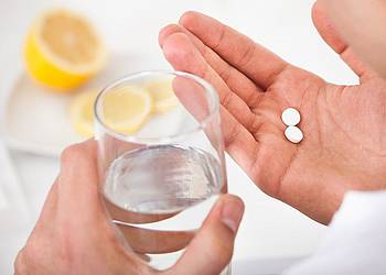 Frauenhände halten Antibiotika-Tabletten und ein Glas Wasser. 