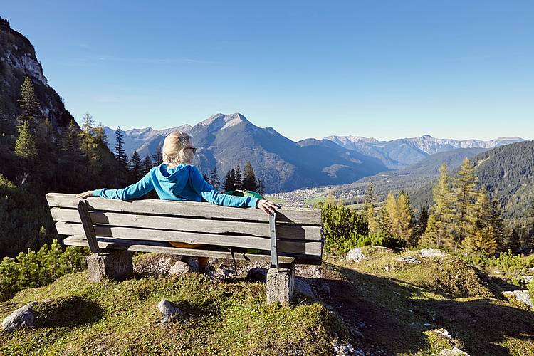 Frau mit leichtem Rheuma ruht sich bei Wanderung auf einer Bank aus. 